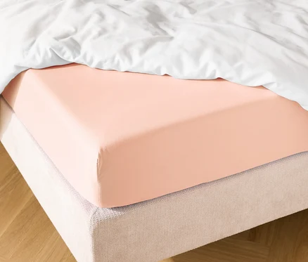 Bett mit lachsfarbenem Spannbettlaken und weißer Bettdecke.