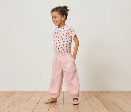 Ein junges Mädchen steht auf einem Holzboden und trägt ein rosa Erdbeer-T-Shirt und eine rosafarbene Hose.