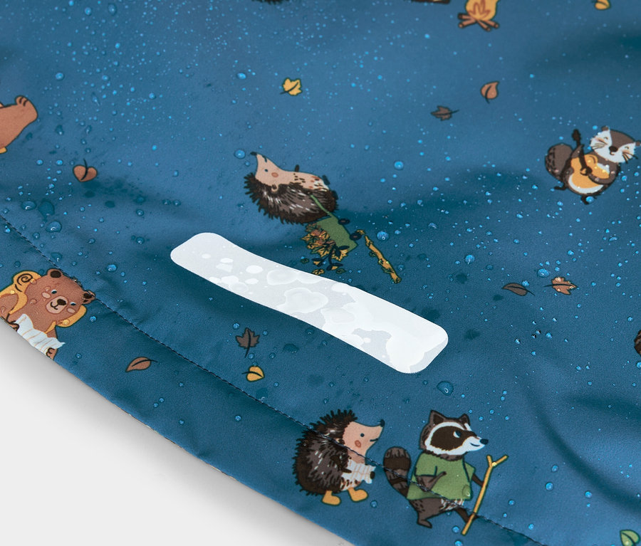 Nahaufnahme eines blauen Stoffes mit Igel-, Bären- und Waschbärmuster, Wassertropfen und einem weißen reflektierenden Streifen.