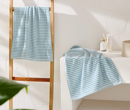 Ein blau-weiß gestreiftes Handtuch hängt an einer Holzleiter. Ein weiteres Handtuch liegt neben einem beigen Waschbecken.