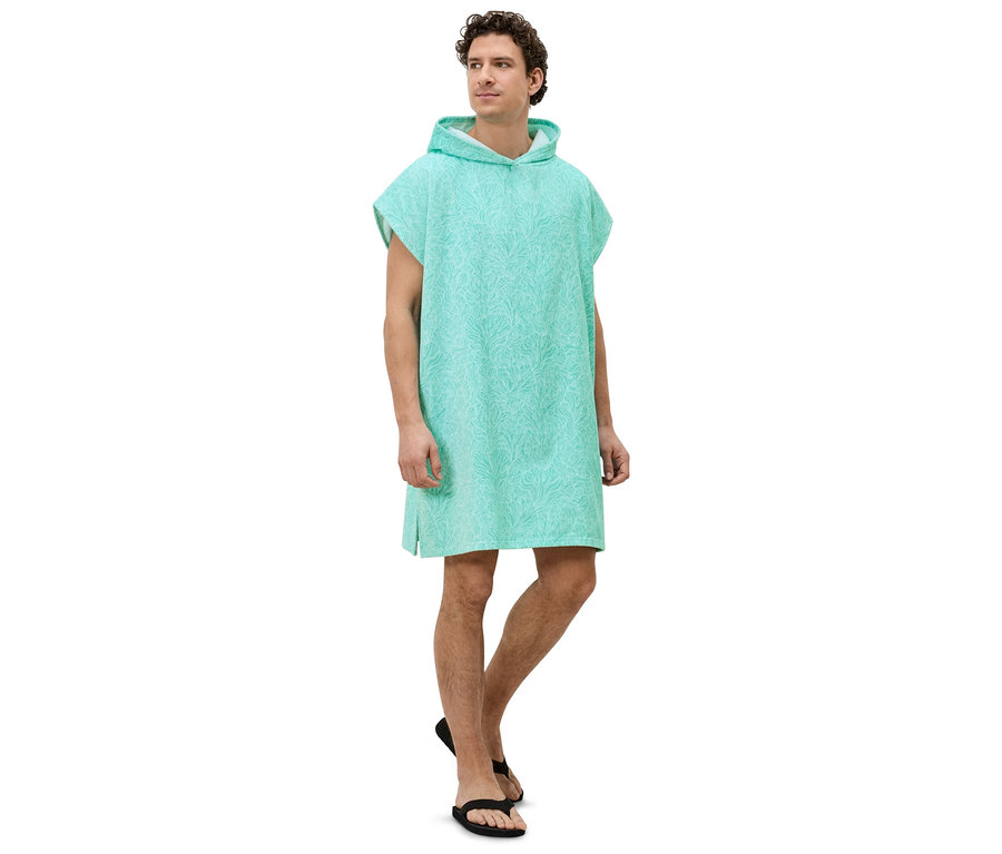 Ein Mann steht seitlich in einem türkisfarbenen, gemusterten Kapuzenponcho und schwarzen Sandalen.