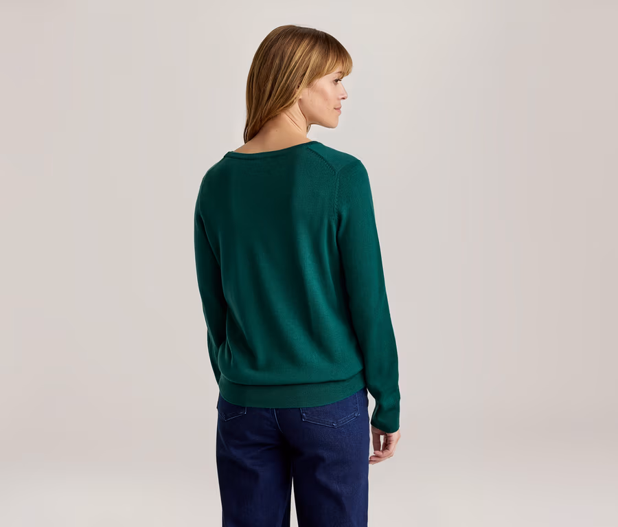 Frau von hinten, leicht nach rechts gedreht, trägt einen grünen Langarmpullover und eine dunkelblaue Jeans.