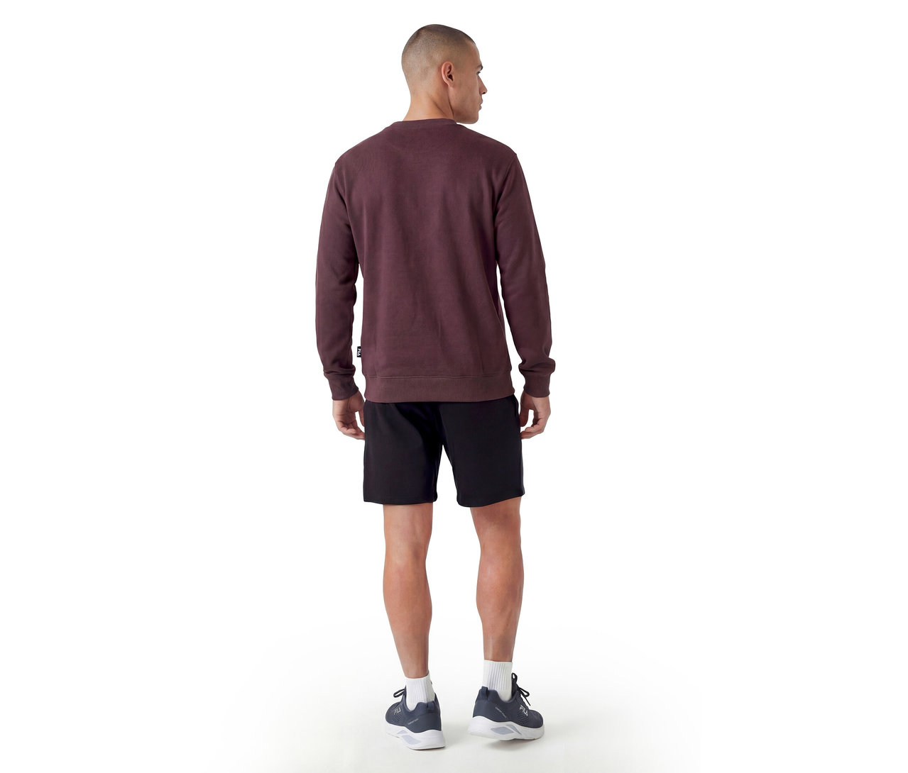Mann steht mit dem Rücken zum Betrachter, trägt ein bordeauxrotes Rundhals-Sweatshirt, schwarze Shorts, weiße Socken und dunkle Sportschuhe.