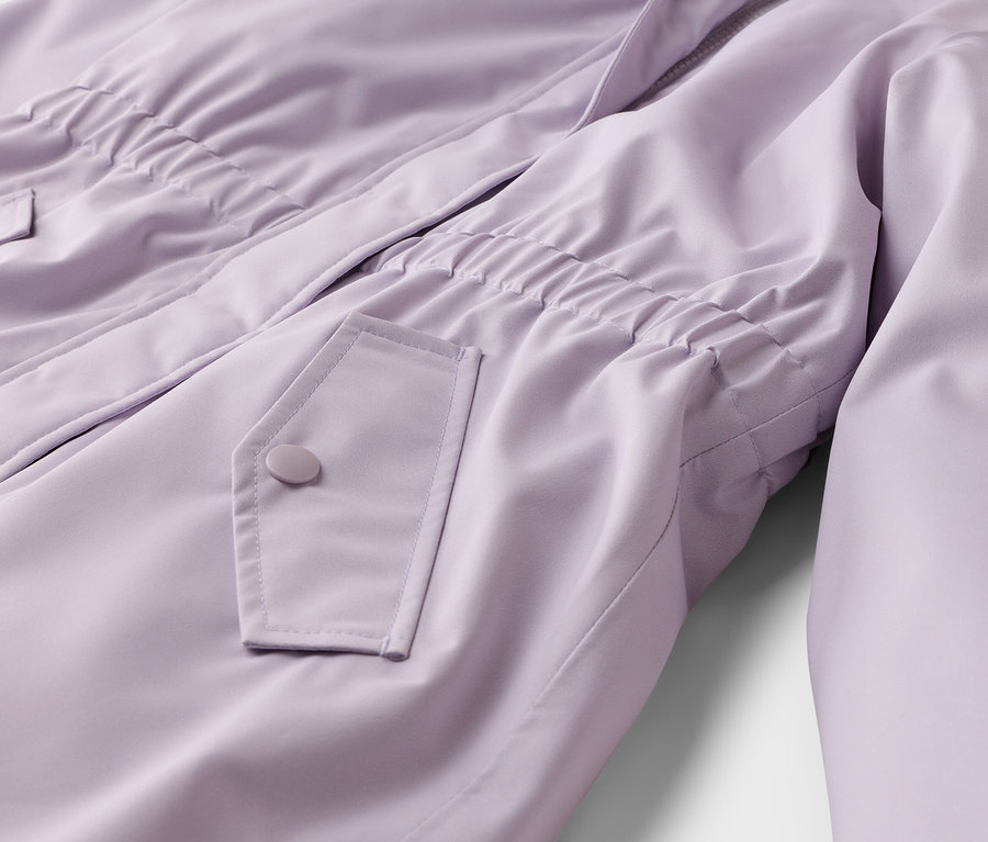 Nahaufnahme einer hellvioletten Jacke mit elastischem Bund, einer Pattentasche mit Knopf und einem teilweise sichtbaren Reißverschluss.