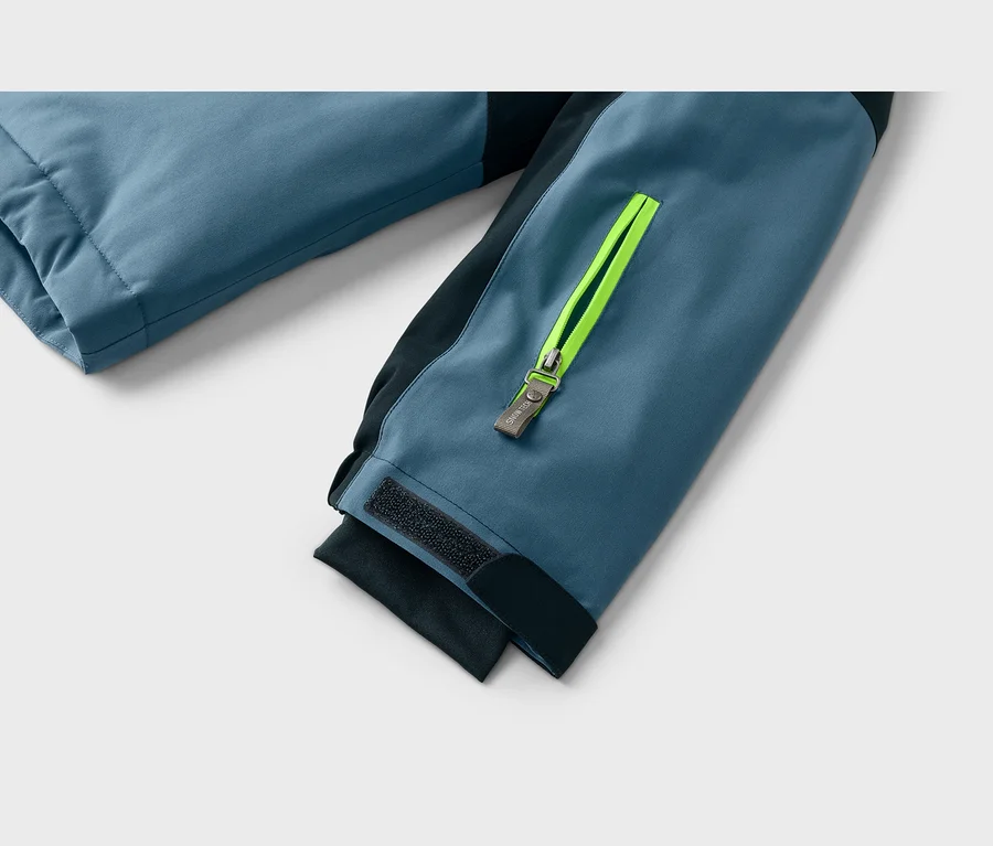 Nahaufnahme eines blau-schwarzen Jackenärmels mit neongelbem Reißverschluss und „SWING“-Zipper am Unterarm sowie einem schwarzen Klettverschluss am Ärmelbündchen.