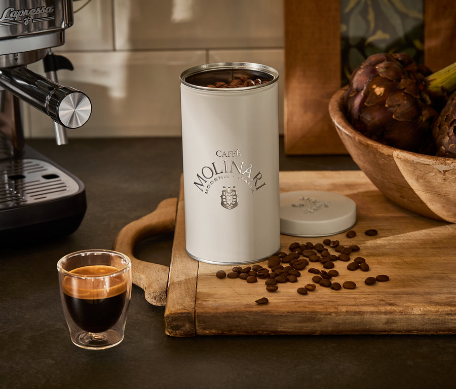Espressomaschine neben Tasse und Caffe Molinari Dose auf einem Holzbrett.