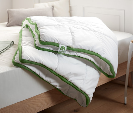 Auf einem Bett liegt ein weißes irisette® greenline Steppbett mit Klimaband.