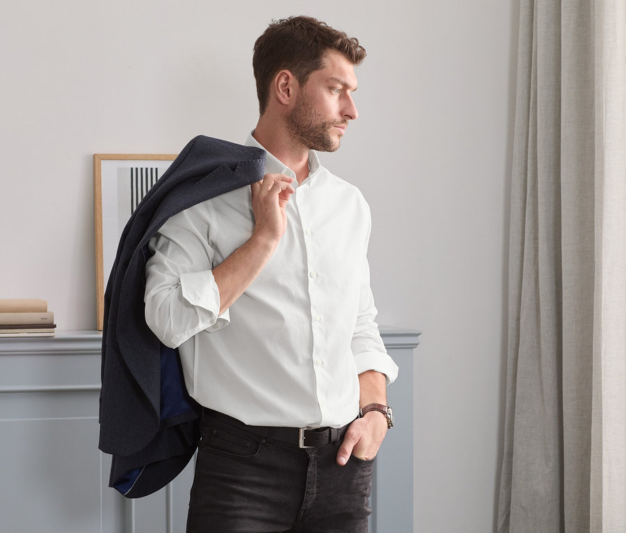 Mann mit braunen Haaren und Bart trägt ein Sakko über der Schulter und ein weißes Oxford-Hemd in Comfort Fit.