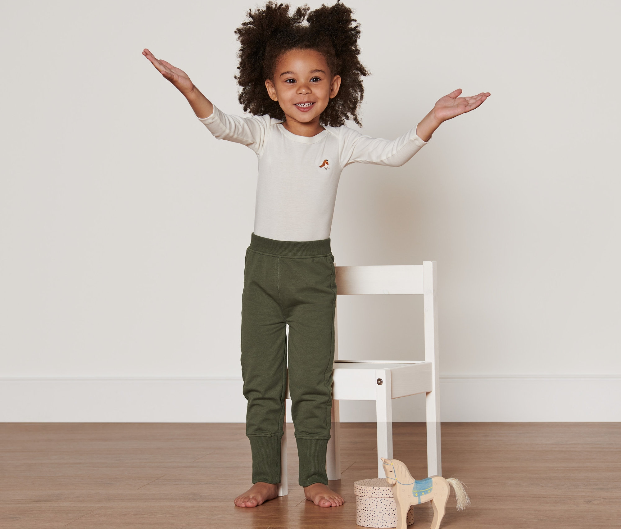 Ein Mädchen steht mit ausgestreckten Armen und trägt 2 Sweathosen.