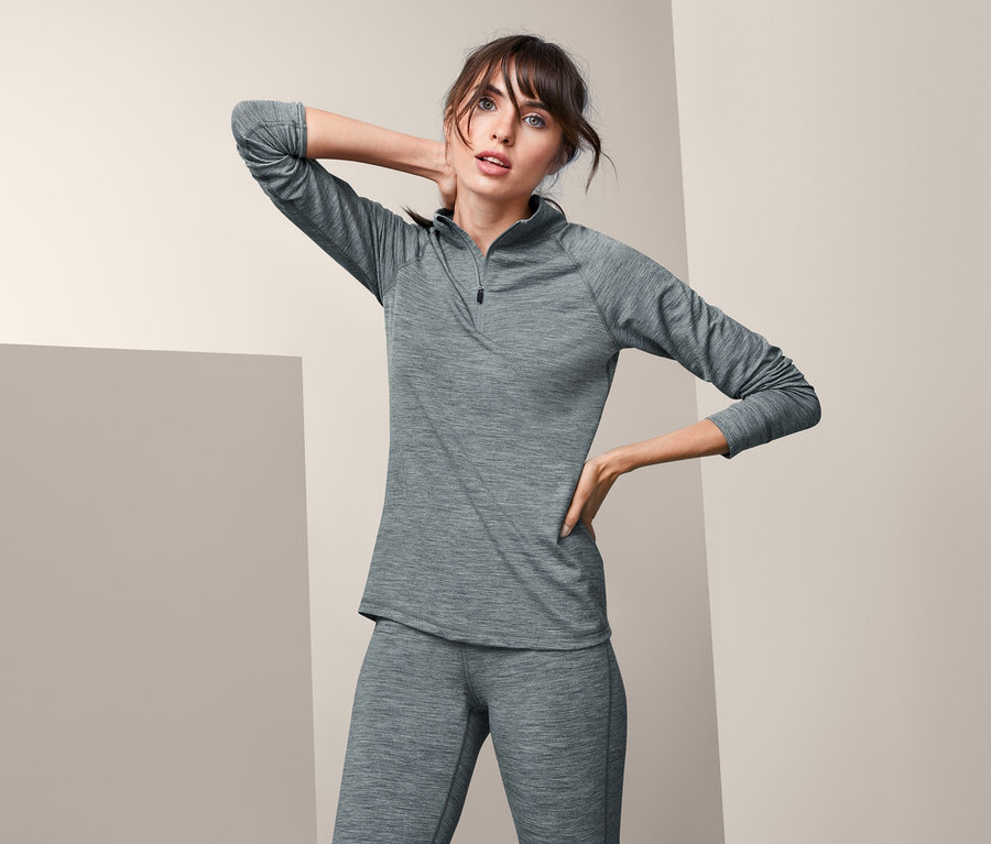 Frau posiert in grauem Funktionsshirt mit Merinowolle und Hose.