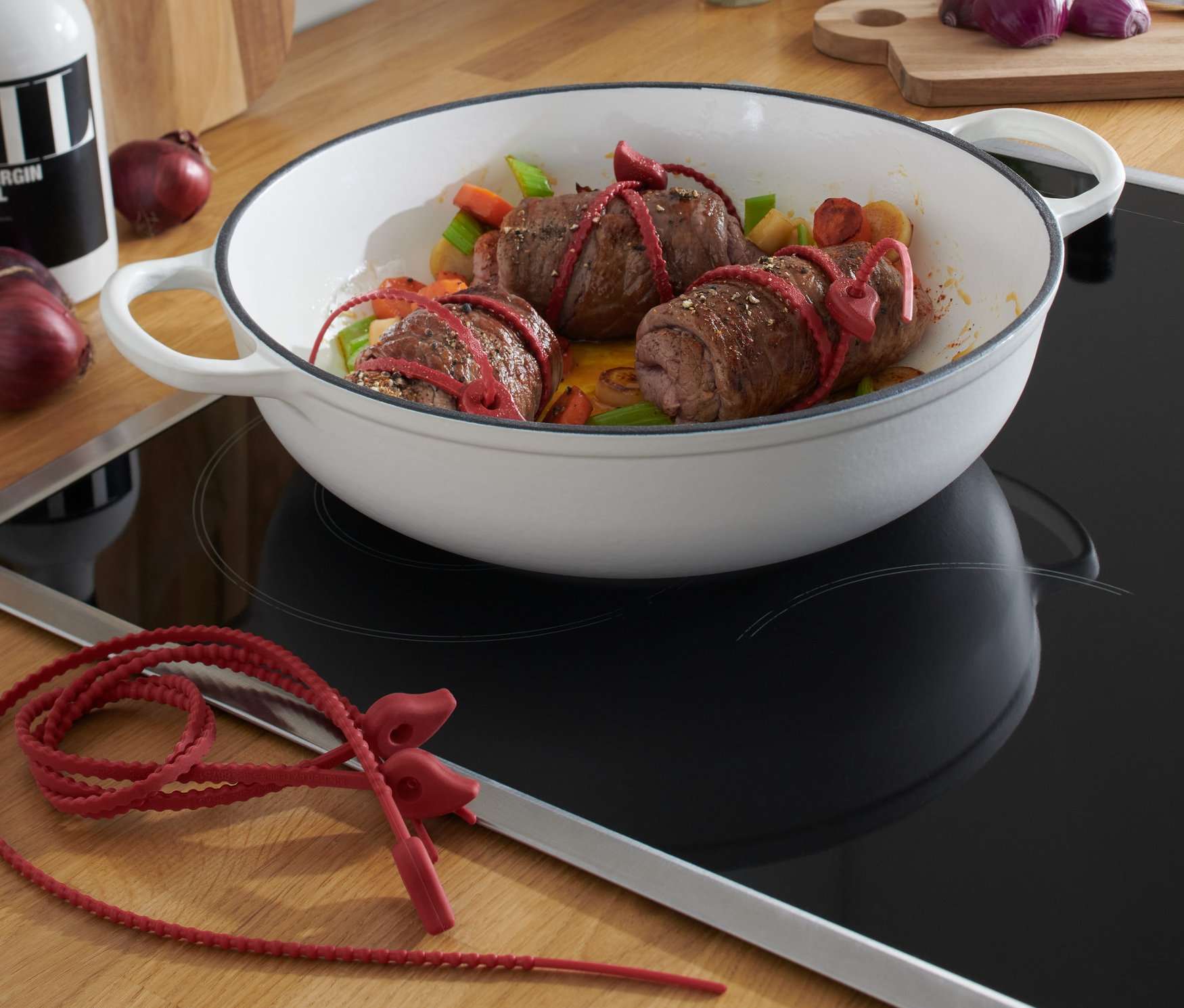 Drei Fleischrouladen, mit 6 Silikonbändern fixiert, liegen in einer weißen Pfanne.