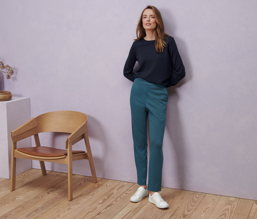 Frau trägt Ledersneaker, dunkelblauen Merino-Feinstrickpullover und Joggpants.