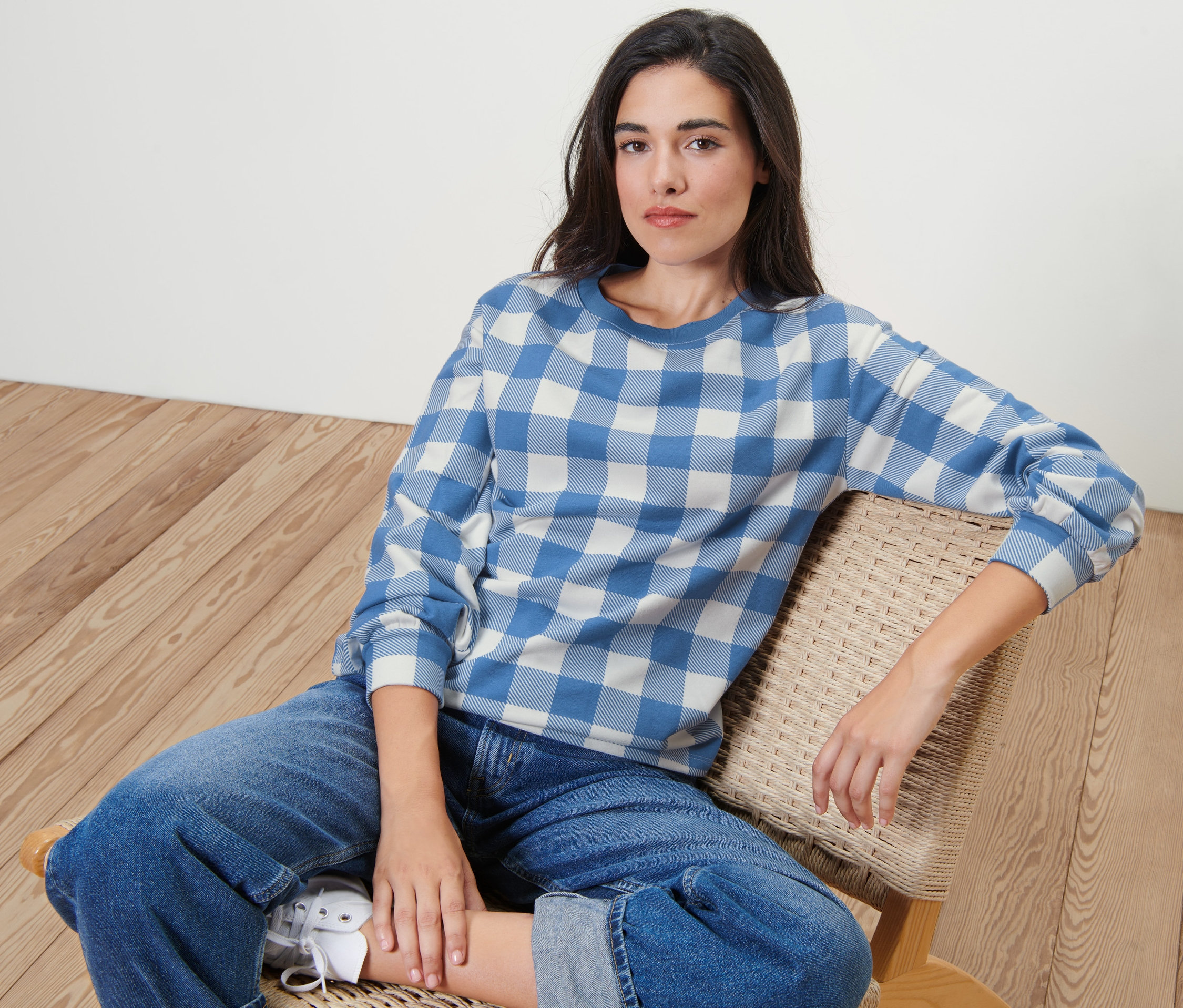 Frau sitzt auf einem Stuhl und trägt ein kariertes Sweatshirt.