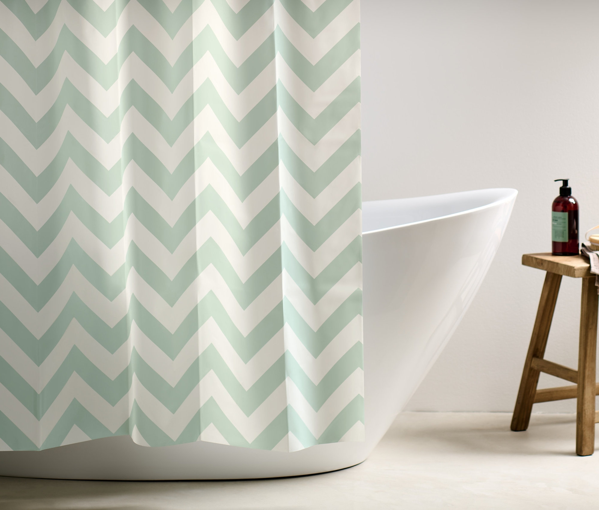 Ein Duschvorhang mit einem Zickzackmuster in Weiß und Hellgrün verdeckt einen Teil einer weißen Badewanne.