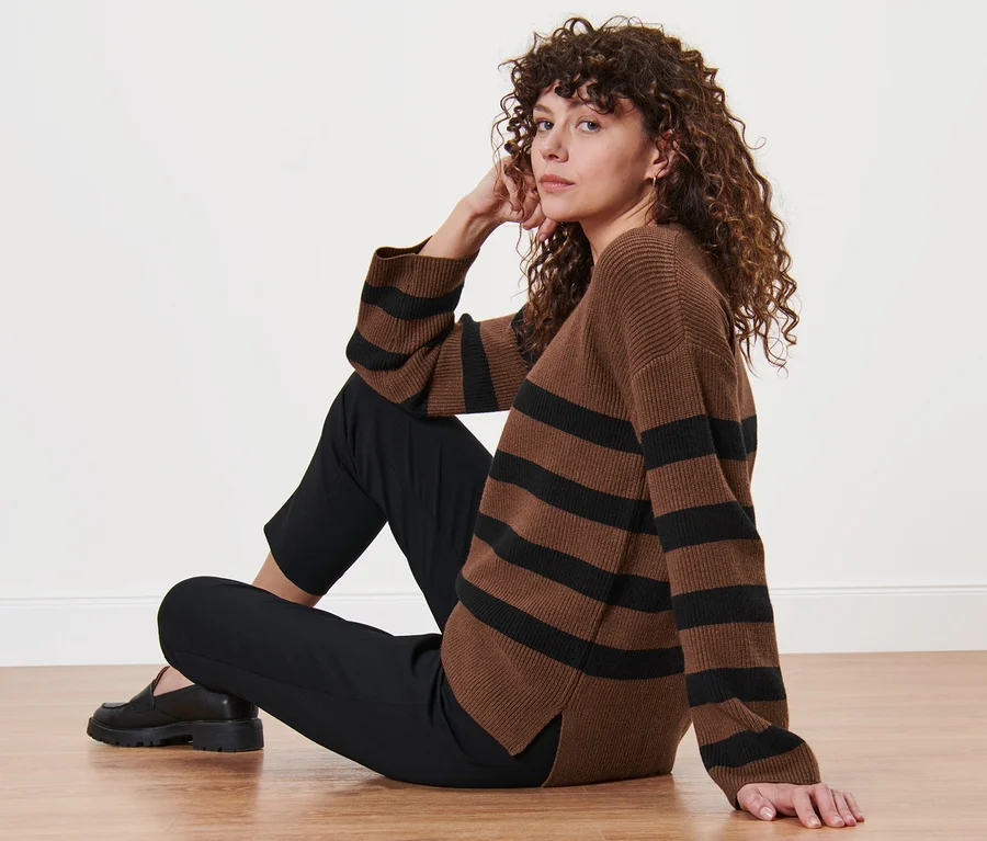 Frau sitzt auf dem Boden und trägt einen gestreiften Strickpullover.