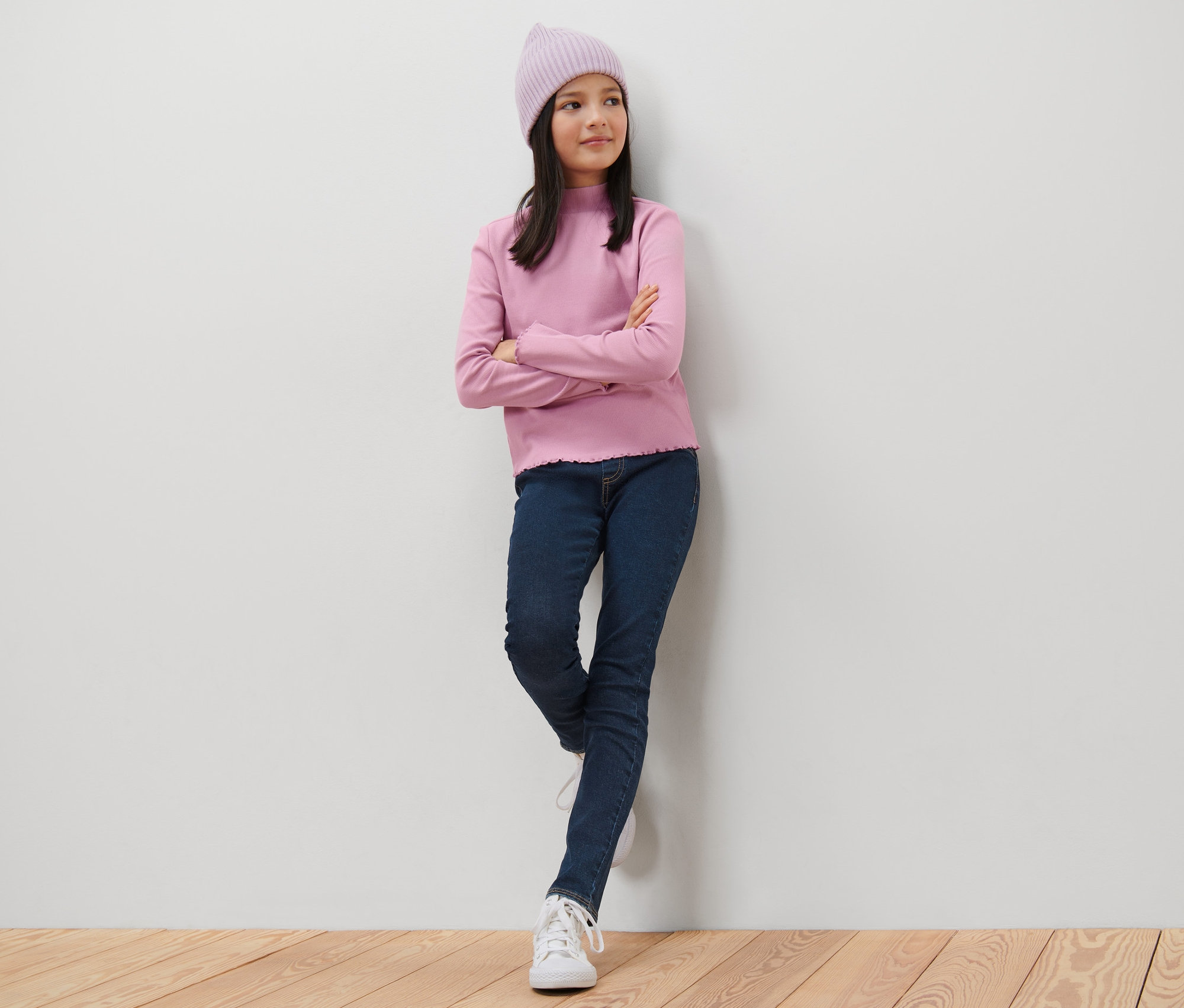 Mädchen mit rosa Pullover und dunkelblauen Kinder-Treggings – Fit »Jule« lehnt an der Wand.