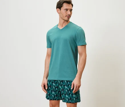 Mann trägt ein Shorty-Pyjama-Set mit einem kurzärmeligen Oberteil und bedruckten Shorts.