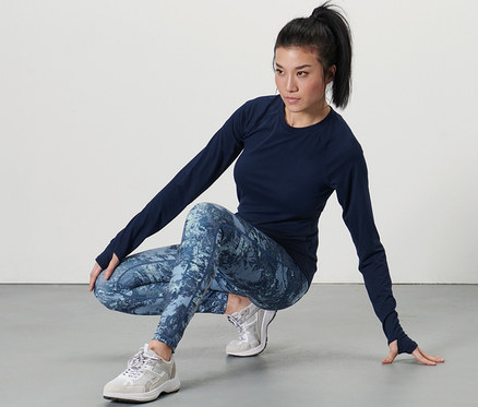 Frau in dunklem Oberteil und Sporttight, dunkelblau/mint, posiert in der Hocke.