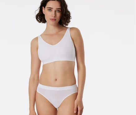 Eine Frau mit kurzen dunklen Haaren trägt einen weißen BH und einen weißen SCHIESSER Rio Slip.