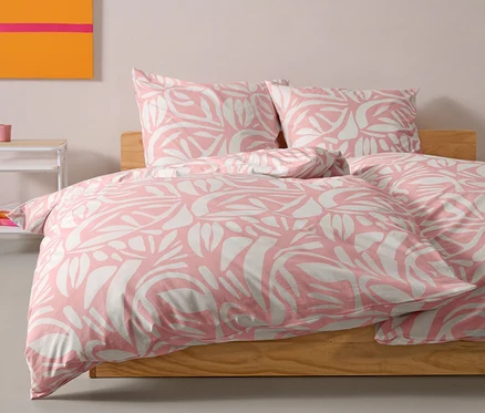 Rosa Renforcé-Bettwäsche in Normalgröße liegt auf einem Bett. Zwei Kissen liegen hinter der Bettdecke.