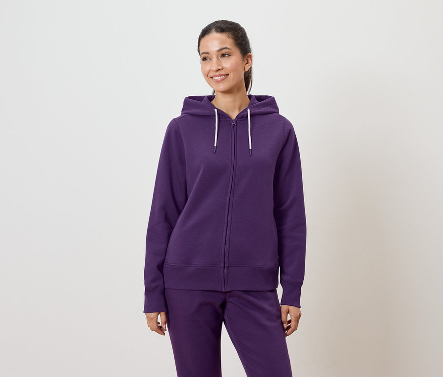 Eine Frau trägt einen violetten Kapuzenpullover und eine Hose.