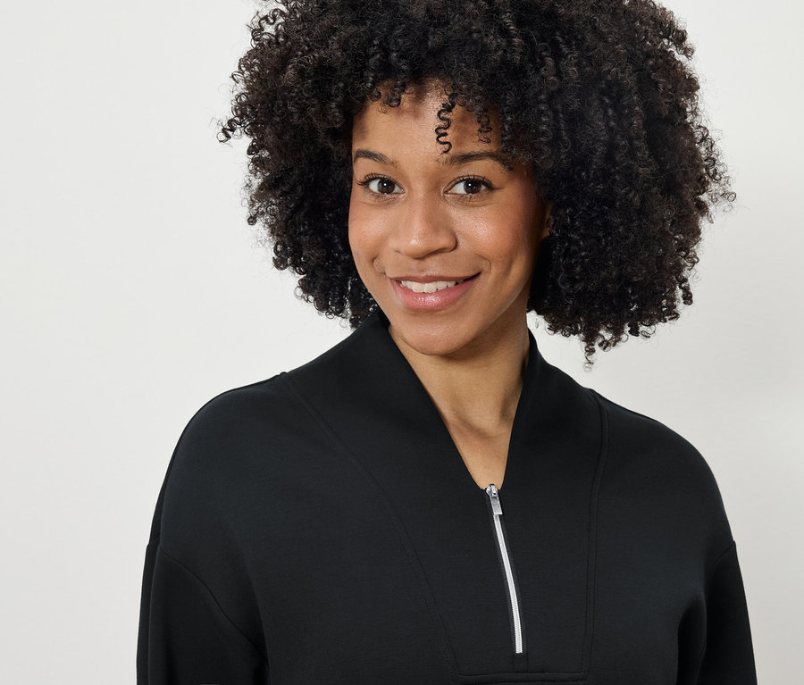 Porträt einer lächelnden Frau mit Afro-Frisur in einem schwarzen Reissverschluss-Sweatshirt.