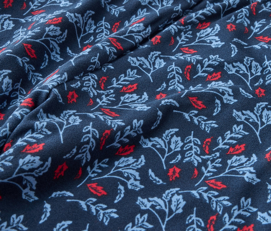Nahaufnahme eines dunkelblauen Stoffes mit einem Aufdruck aus roten und hellblauen Blättern.