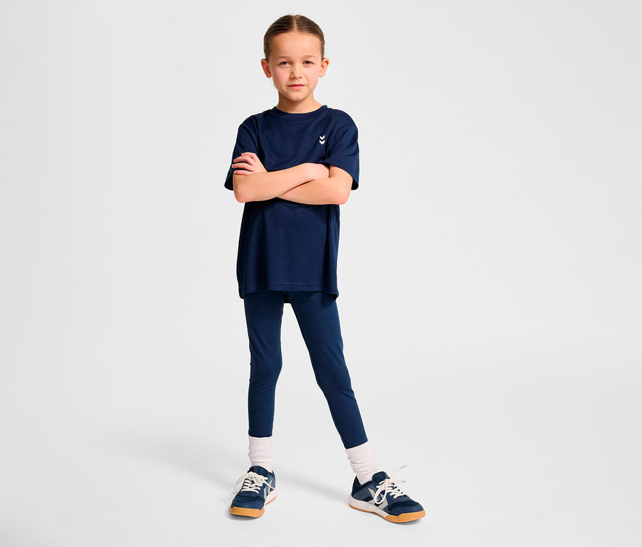 Mädchen posiert in dunkelblauem HUMMEL HMLJR pulse Training-T-Shirt und Leggings.