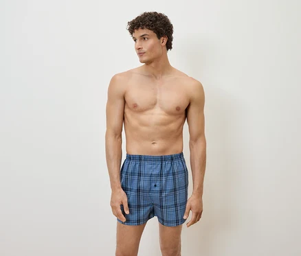 Mann posiert in blau karierten Boxershorts vor einem weißen Hintergrund.