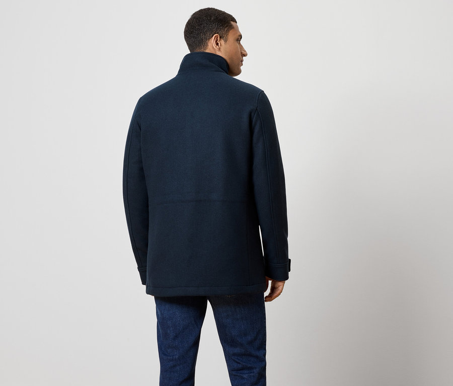 Mann von hinten, trägt einen dunkelblauen Mantel und Jeans.