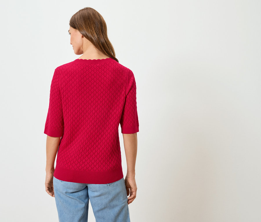 Rückansicht einer Frau mit langen braunen Haaren, die einen roten Pullover und blaue Jeans trägt.