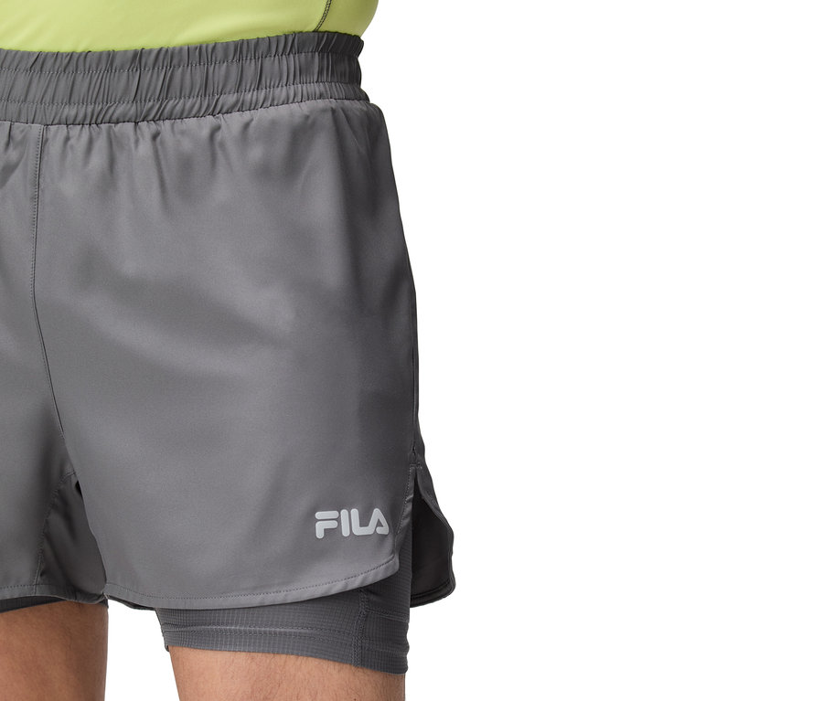Nahaufnahme einer Person, die graue Fila-Shorts mit Gummizug und Fila-Logo trägt.
