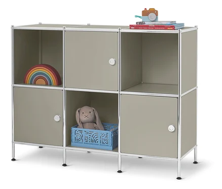 Ein niedriges Regal mit sechs Fächern steht vor einem weißen Hintergrund. In den Fächern befinden sich ein Holzregenbogen, ein Spielzeughase in einem blauen Korb und Bücher.