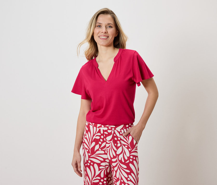 Frau trägt ein rotes T-Shirt und eine weiße Hose mit rotem Muster.