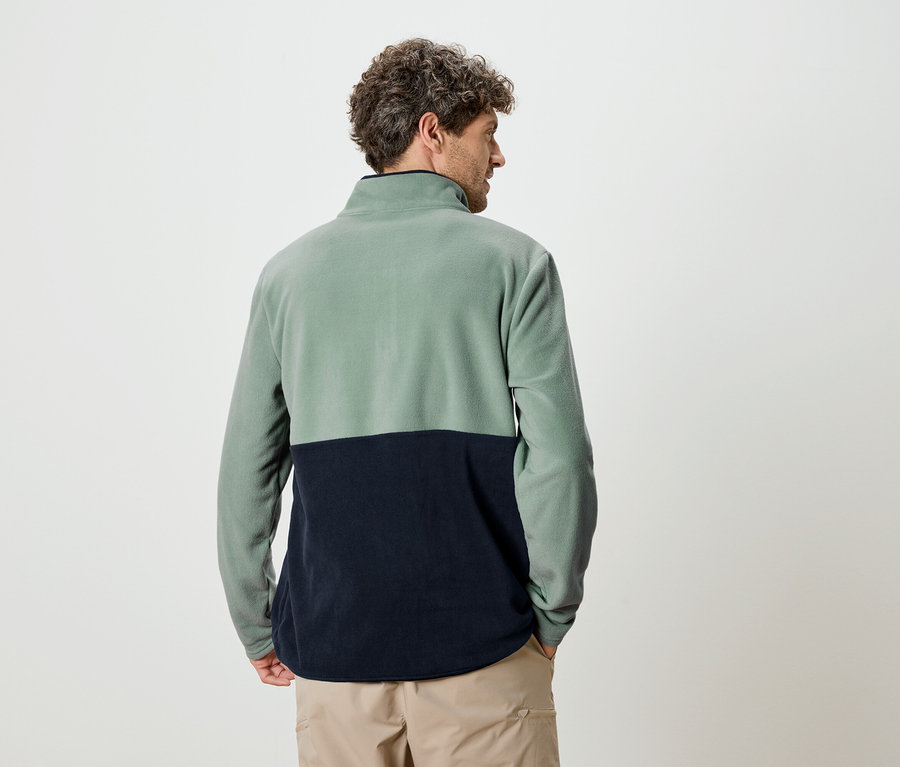 Mann von hinten in einem zweifarbigen Fleece-Pullover in Grün und Marineblau und beigen Hosen.