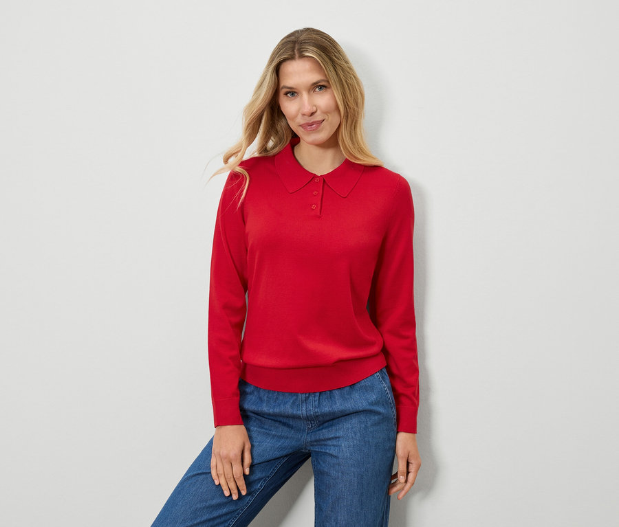 Frau trägt einen roten Pullover und blaue Jeans.