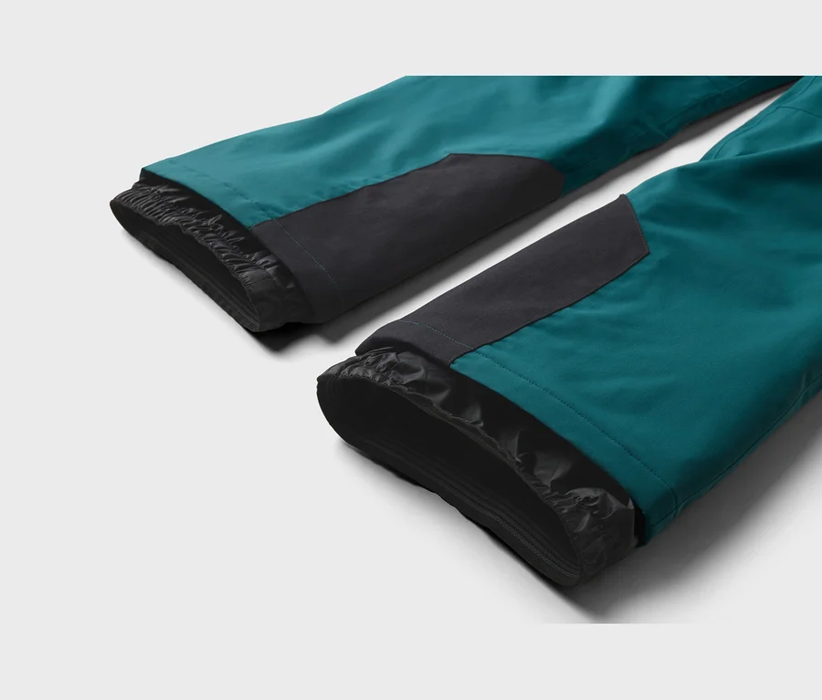 Nahaufnahme der Unterseite von zwei türkis-schwarzen Skihosenbeinen mit schwarzen Innenmanschetten und verstärkten schwarzen Patches.