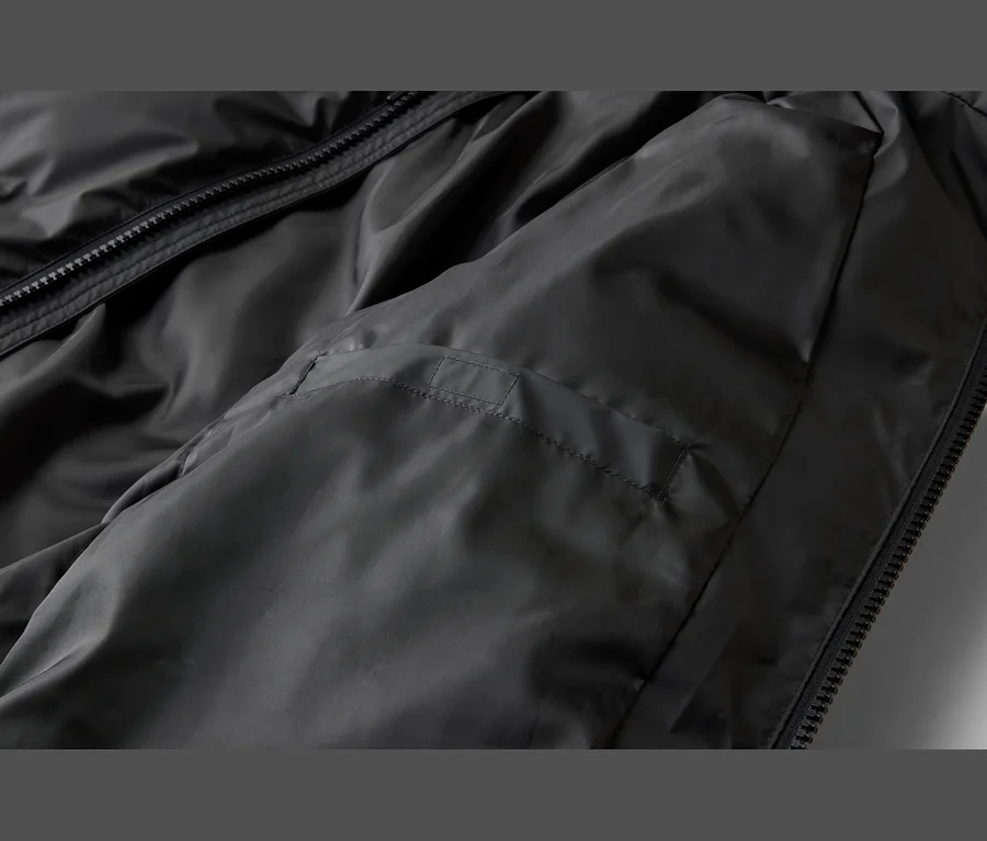 Nahaufnahme einer schwarzen Jacke aus glattem, leicht glänzendem Stoff, mit schwarzem Reißverschluss und einer horizontalen Naht auf der linken Seite.