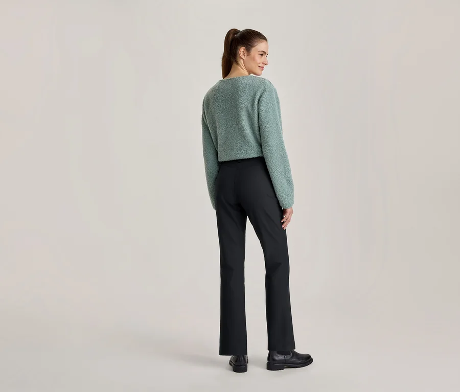 Frau von hinten, leicht zur Seite gedreht, trägt einen hellgrünen flauschigen Pullover, schwarze Hose und schwarze Schuhe.