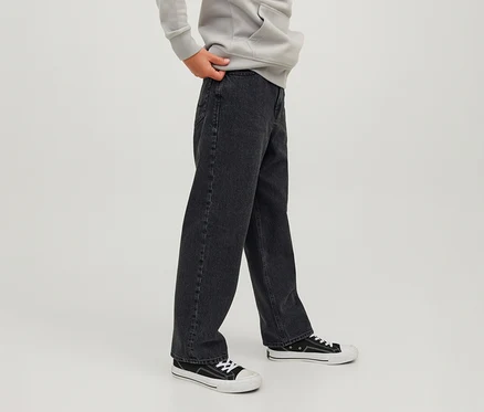 Person trägt schwarze Jack&Jones JJOrginial Alex Jeans, einen hellgrauen Hoodie und schwarz-weiße Sneaker, eine Hand hält den Hosenbund der Jeans.