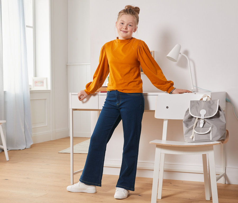 Mädchen steht am Schreibtisch und trägt eine Bootcut-Jeans.