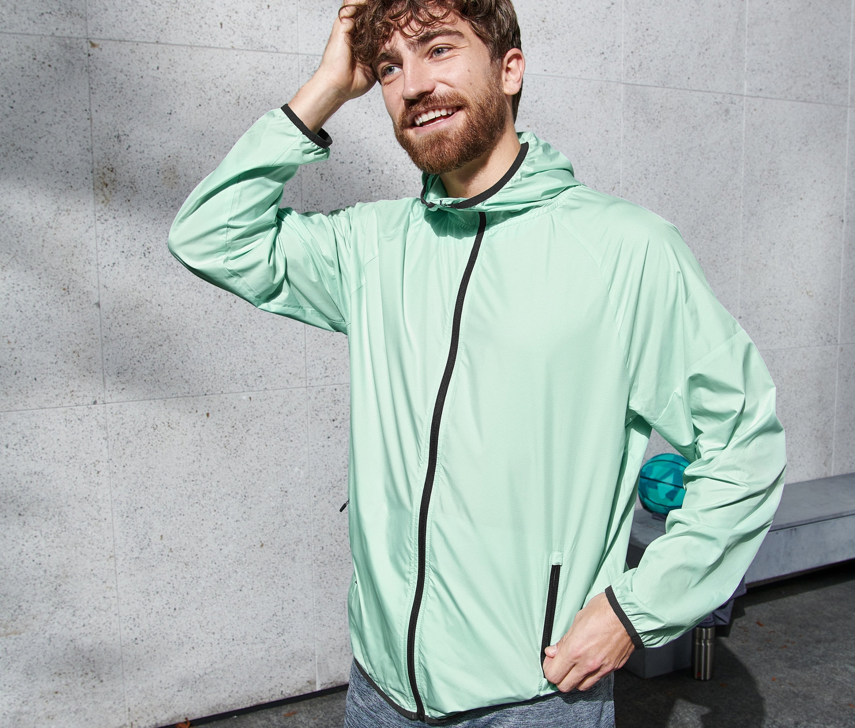 Mann mit Laufjacke in Mint berührt seine Haare.