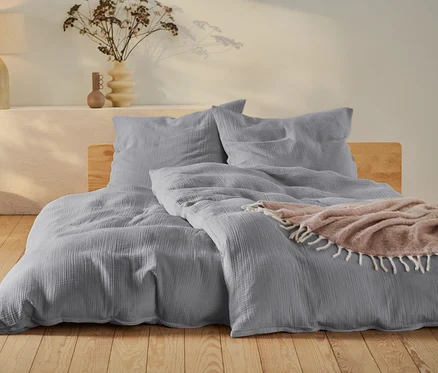Graue Musselin-Bettwäsche in Normal- und Übergröße auf einem Bett.