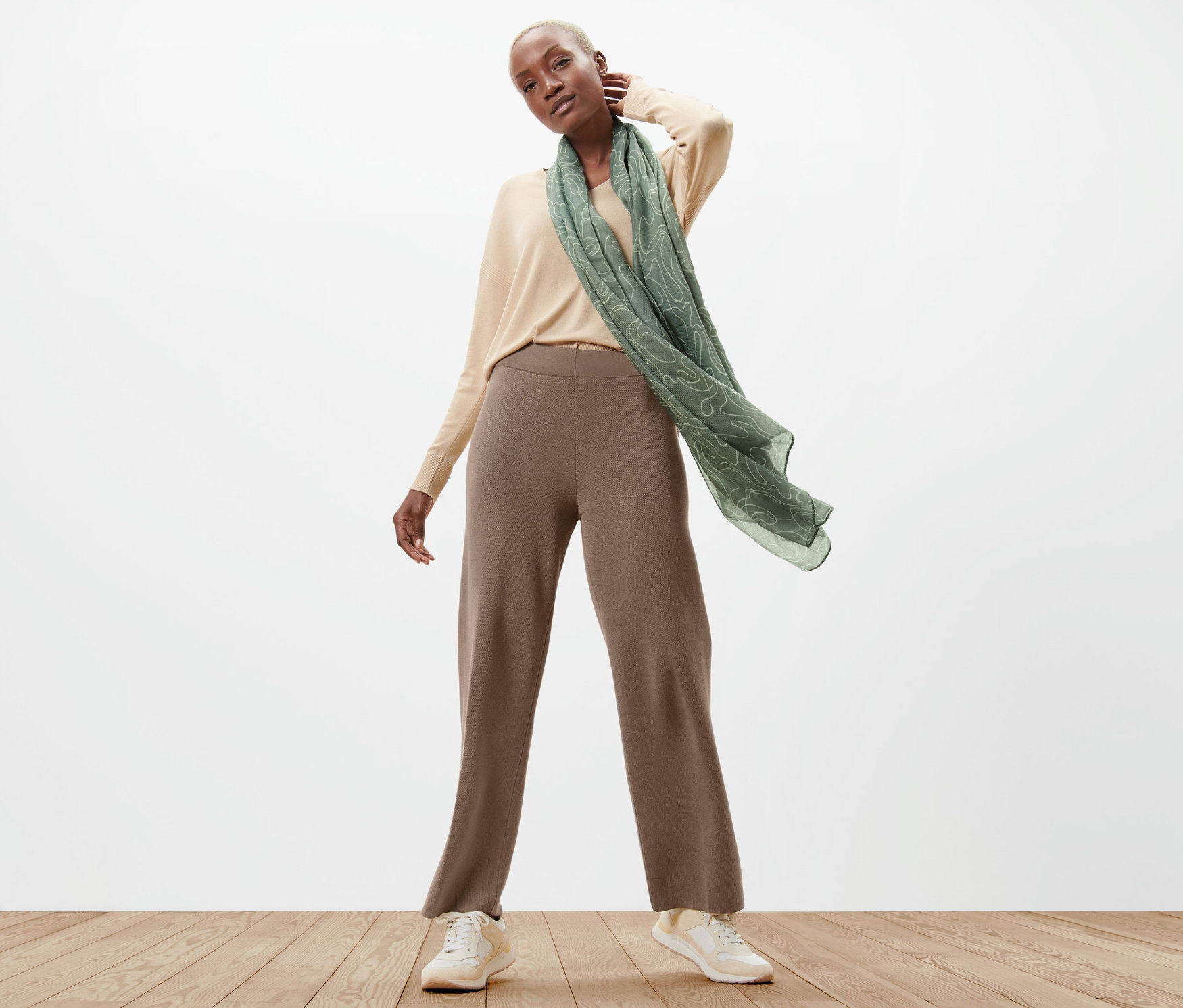Frau posiert in Strickhose, Pullover und Schal.