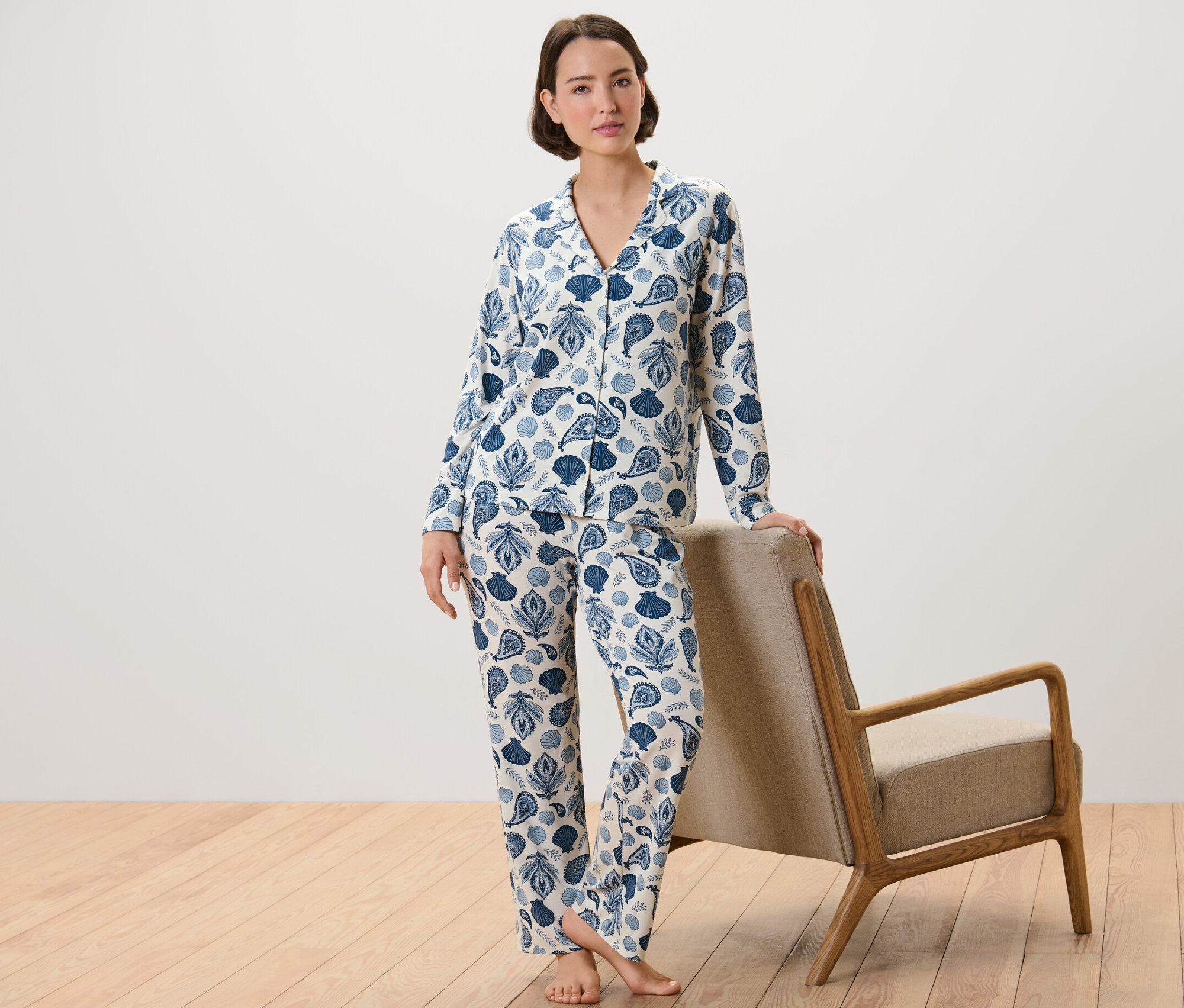 Frau im Pyjama mit Muschel- und Paisley-Print, die an einem Sessel lehnt.