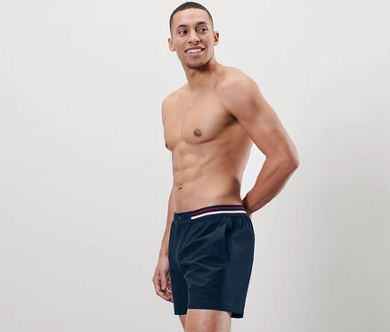 Mann posiert ohne Hemd in Badeshorts.