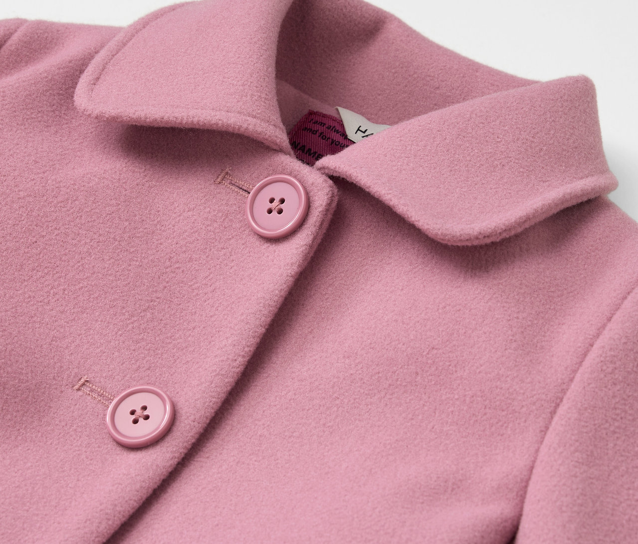 Detailaufnahme eines rosa Mantels mit Kragen und Knöpfen.