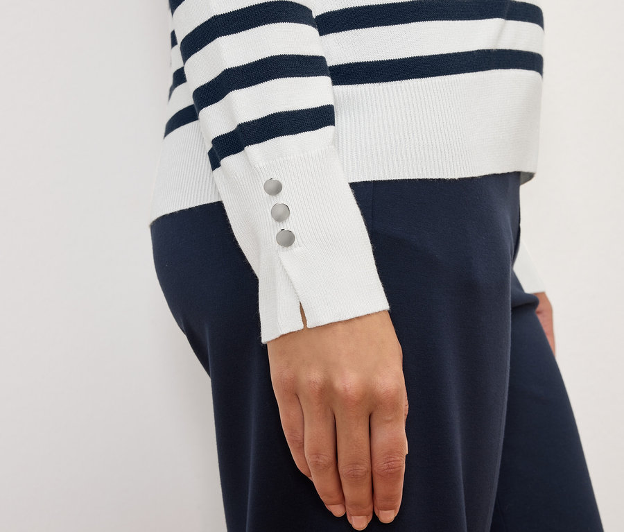 Frau trägt einen gestreiften Langarmpullover mit Knöpfen an den Manschetten und eine marineblaue Hose.