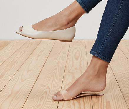 Beine einer Frau in Jeans, ein Bein in einem cremefarbenen Peeptoe-Ballerina, das andere in einer Riemchensandalette. 1 Paar Einlegesohlen mit Fußbett in der Sandalette.