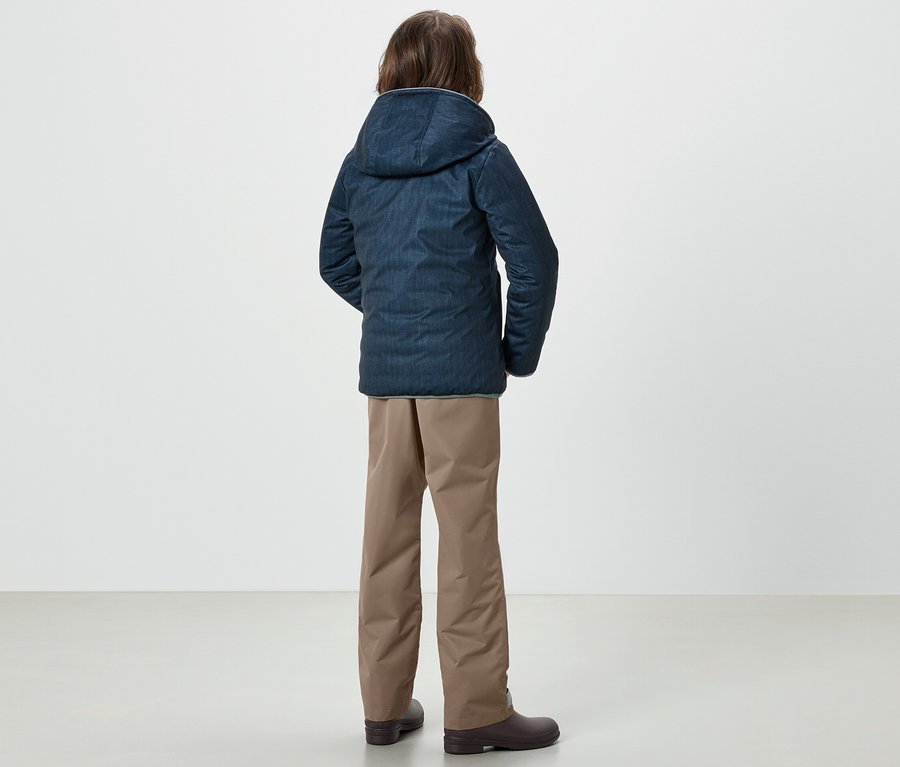Ein Junge steht mit dem Rücken zur Kamera und trägt eine blaue Jacke und eine Kinder-Regenhose.